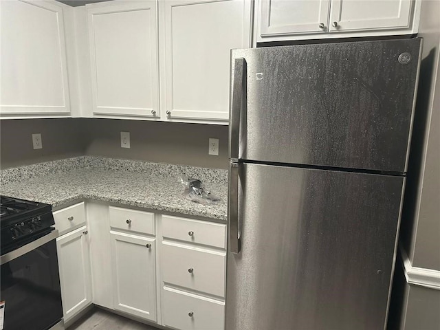 kitchen with gas stove, light stone counters, white cabinets, and freestanding refrigerator