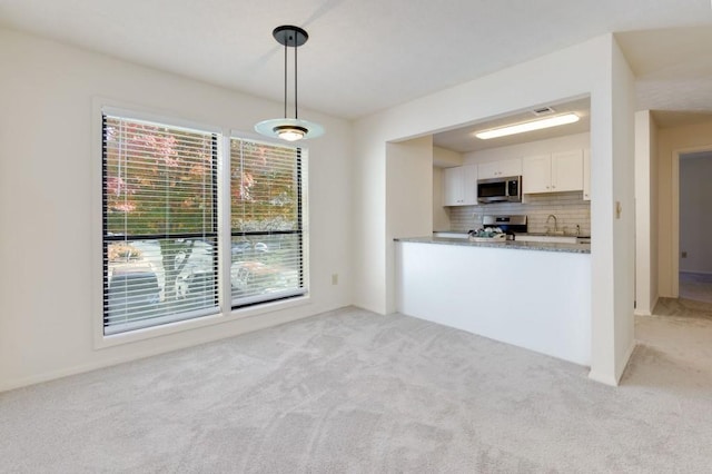 kitchen with light carpet, decorative light fixtures, backsplash, white cabinetry, and appliances with stainless steel finishes