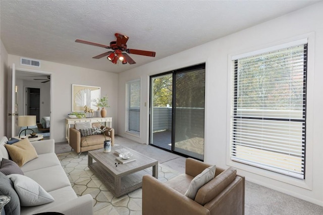 living area with a textured ceiling, a ceiling fan, visible vents, and light carpet