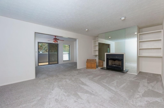 unfurnished living room with a fireplace with raised hearth, baseboards, carpet floors, and a textured ceiling