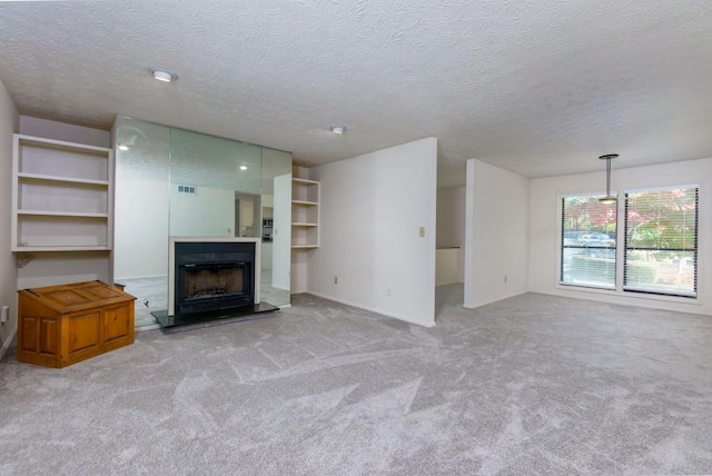 unfurnished living room with a textured ceiling, a fireplace with raised hearth, and carpet flooring