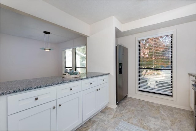 kitchen featuring baseboards, pendant lighting, dark stone countertops, stainless steel refrigerator with ice dispenser, and white cabinets