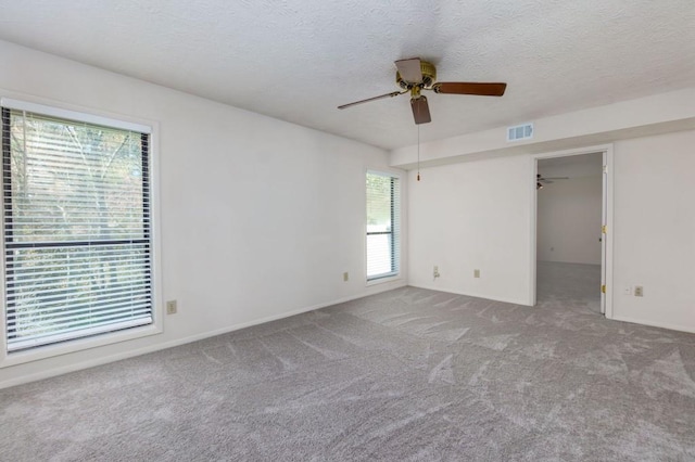 carpeted empty room with visible vents, a healthy amount of sunlight, and a textured ceiling