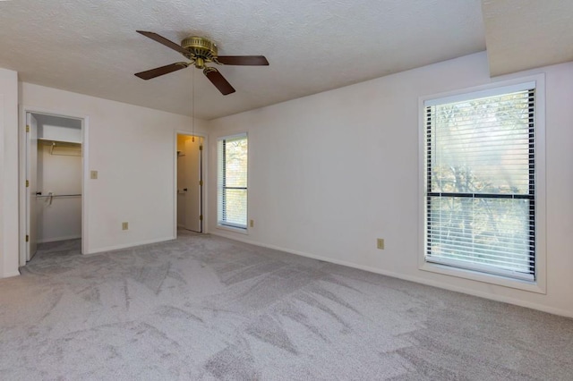 unfurnished bedroom featuring a spacious closet, baseboards, carpet floors, a textured ceiling, and a ceiling fan