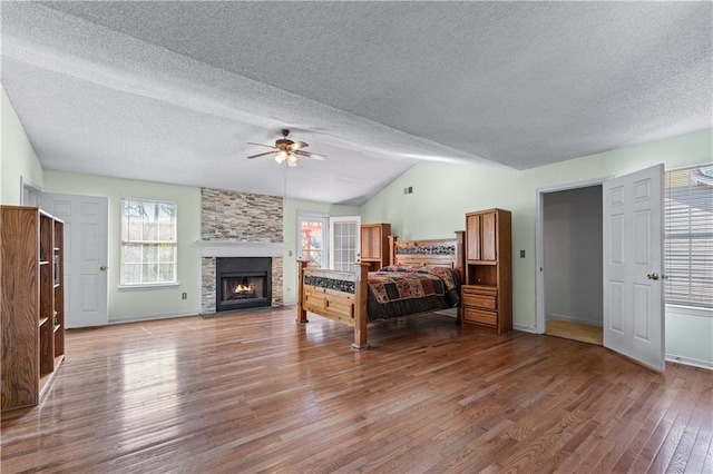 bedroom with a textured ceiling, wood finished floors, a large fireplace, lofted ceiling, and ceiling fan