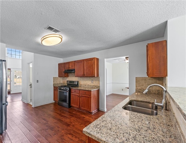 kitchen featuring visible vents, a sink, under cabinet range hood, stainless steel appliances, and dark wood-style flooring