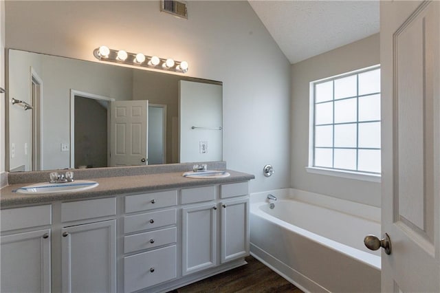 bathroom featuring hardwood / wood-style floors, a textured ceiling, vanity, a bath, and vaulted ceiling