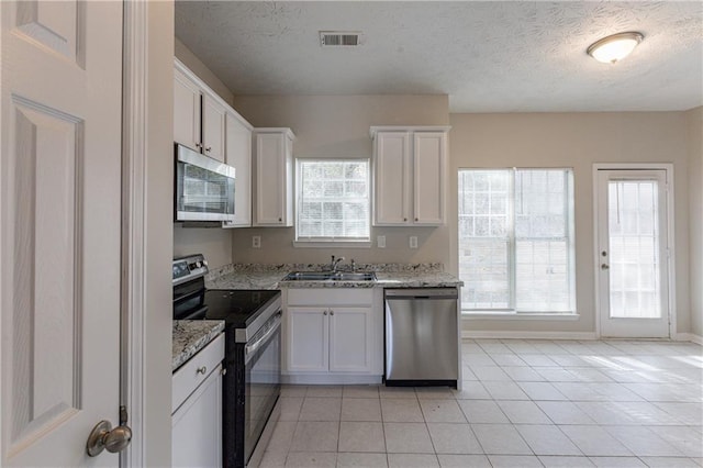 kitchen featuring light tile patterned floors, white cabinets, light stone counters, and appliances with stainless steel finishes