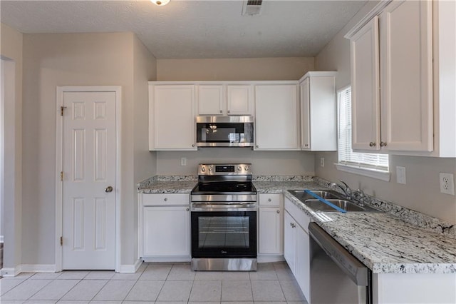 kitchen with light tile patterned floors, white cabinetry, appliances with stainless steel finishes, light stone countertops, and sink