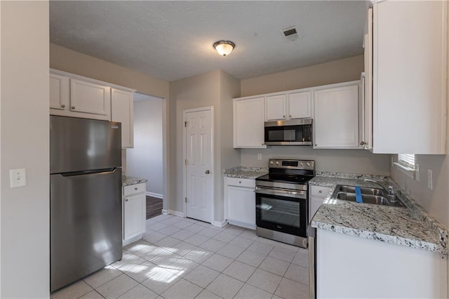 kitchen with light tile patterned floors, sink, stainless steel appliances, and white cabinetry