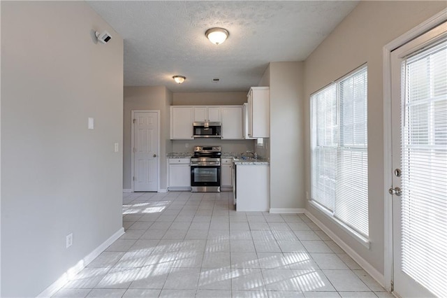 kitchen with light tile patterned floors, white cabinetry, appliances with stainless steel finishes, light stone countertops, and a textured ceiling