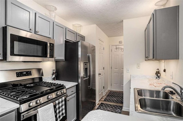 855 Lakeside Cir, Covington, GA 30016 - kitchen with stainless steel appliances, a sink, a textured ceiling, gray cabinetry, and light stone counters