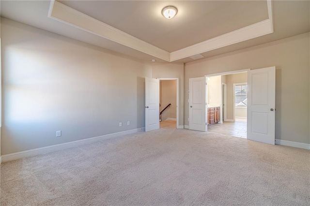 spare room featuring light carpet, a raised ceiling, and baseboards