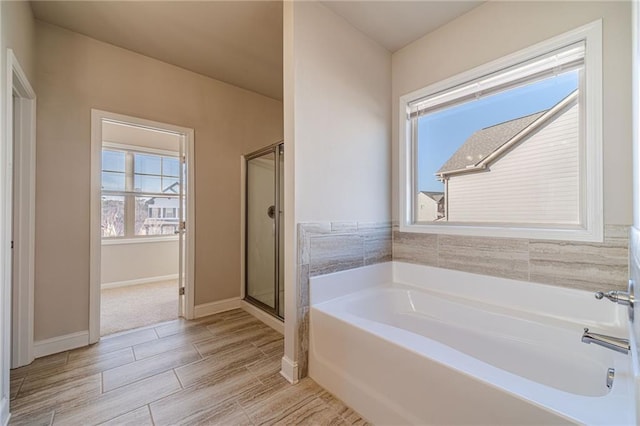 bathroom with a bath, baseboards, and a stall shower