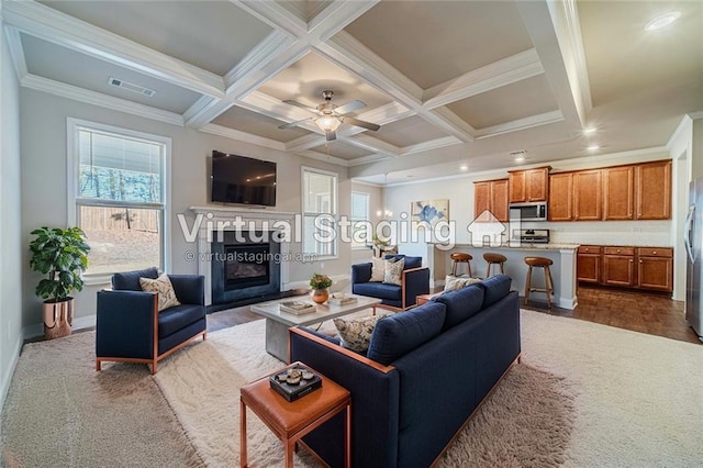 living room featuring beam ceiling, a glass covered fireplace, coffered ceiling, and crown molding