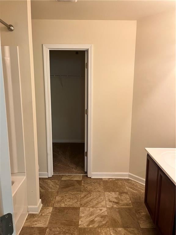 full bathroom with vanity, a tub to relax in, stone finish flooring, baseboards, and a spacious closet