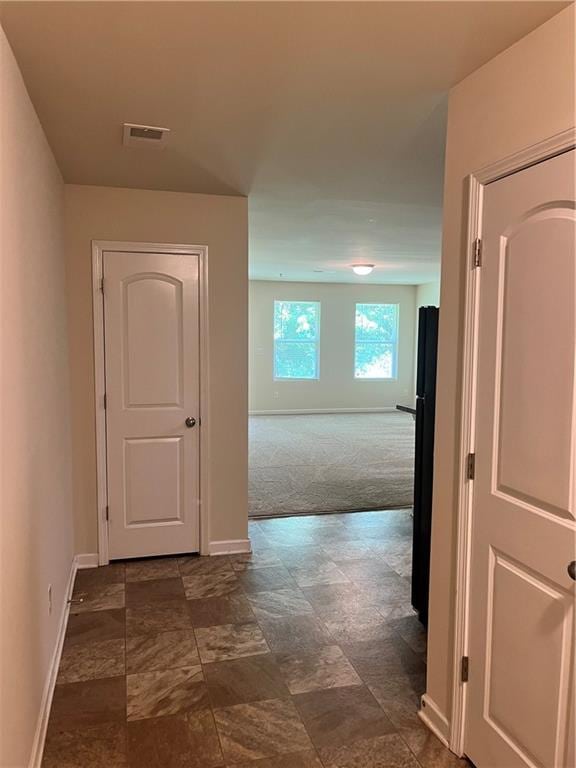 hallway featuring baseboards, visible vents, and dark colored carpet
