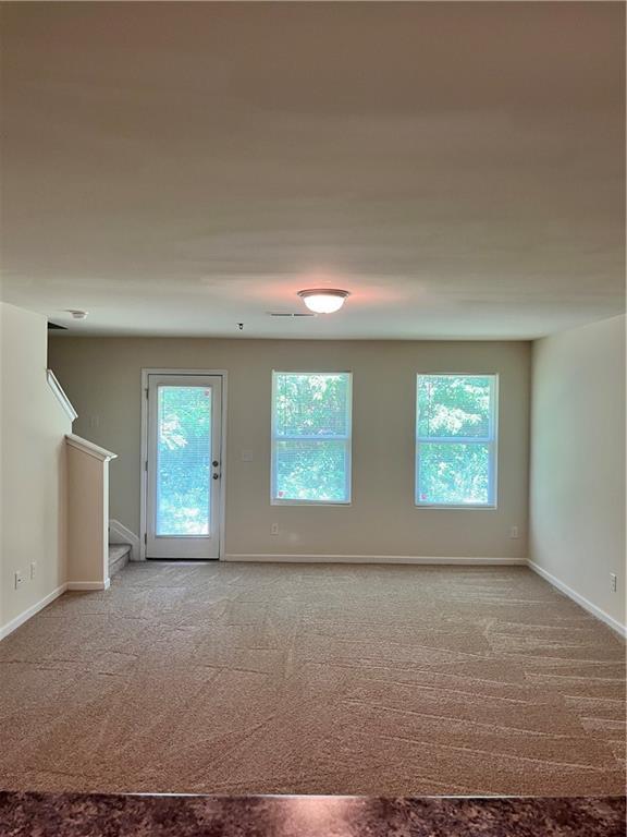 carpeted spare room with a healthy amount of sunlight, stairs, and baseboards