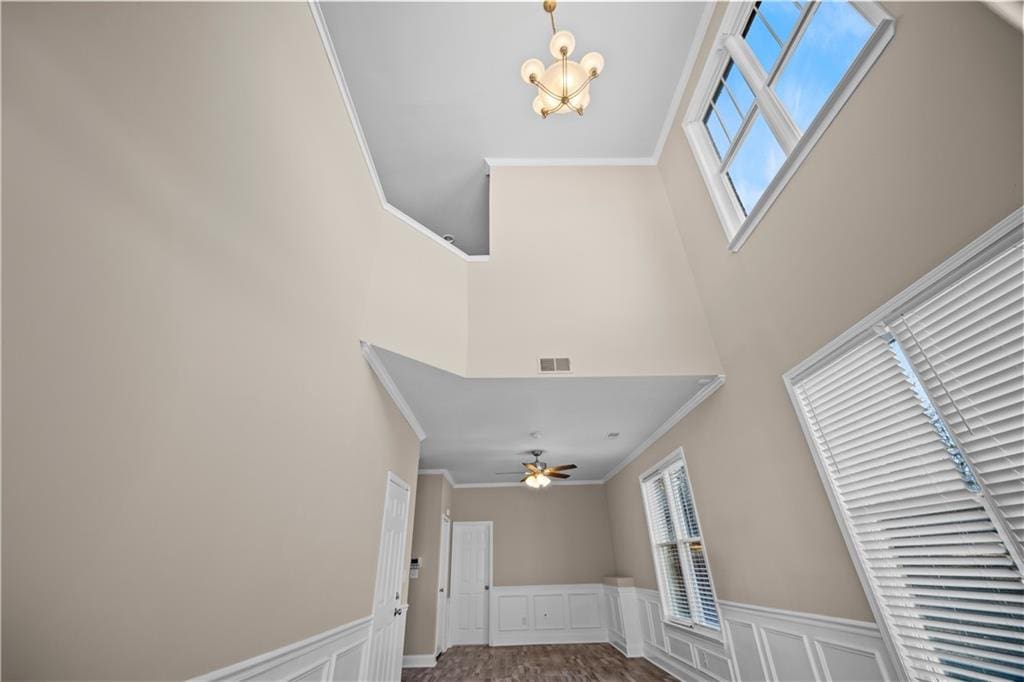 foyer entrance featuring a decorative wall, a wainscoted wall, ceiling fan with notable chandelier, visible vents, and ornamental molding