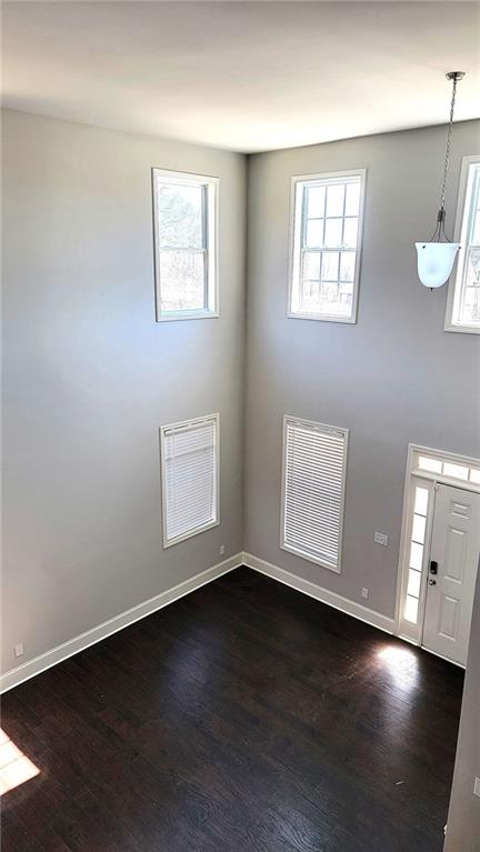 spare room featuring a healthy amount of sunlight, dark wood-style floors, and visible vents