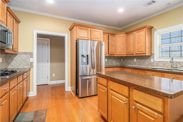 kitchen with crown molding, stainless steel appliances, visible vents, light wood-style floors, and a sink