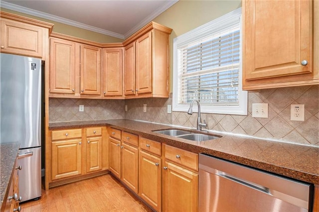 kitchen with a sink, ornamental molding, appliances with stainless steel finishes, dark stone counters, and light wood finished floors