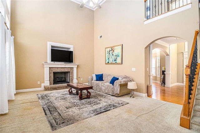 carpeted living area featuring arched walkways, visible vents, stairway, a brick fireplace, and baseboards