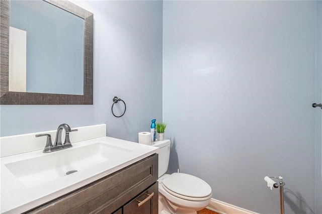 half bathroom featuring baseboards, vanity, and toilet