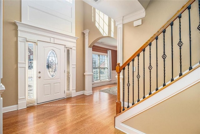 entrance foyer with arched walkways, ornate columns, light wood-style flooring, baseboards, and stairs