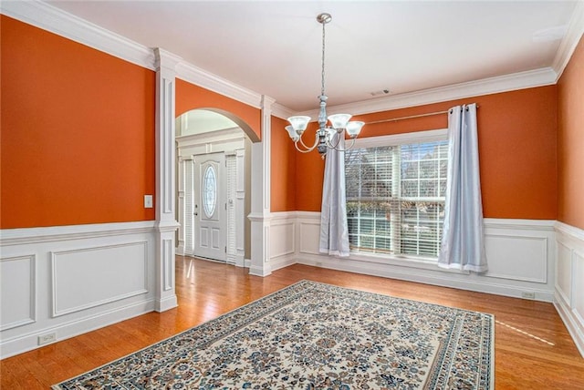 unfurnished dining area with a wealth of natural light, a wainscoted wall, arched walkways, and wood finished floors