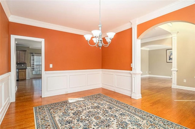 spare room featuring a chandelier, arched walkways, wood finished floors, and crown molding