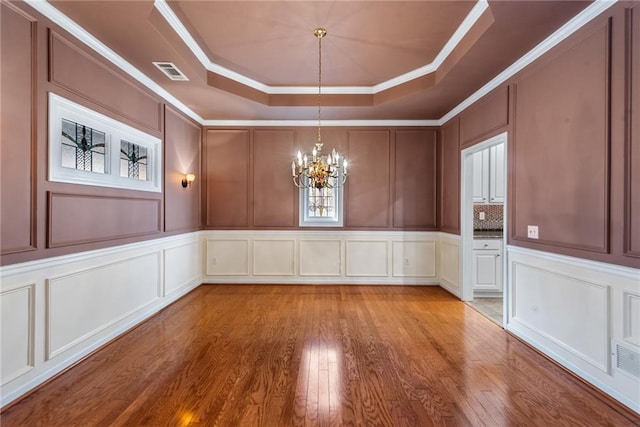 spare room featuring crown molding, a tray ceiling, a chandelier, and light wood-type flooring