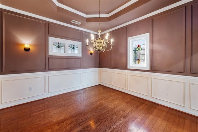 unfurnished dining area with hardwood / wood-style flooring, crown molding, a chandelier, and a tray ceiling