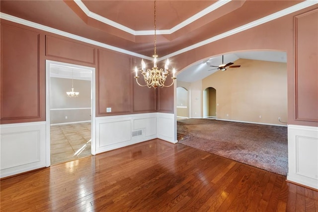 unfurnished dining area featuring a raised ceiling, crown molding, wood-type flooring, and ceiling fan with notable chandelier