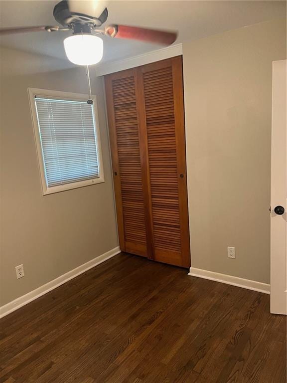 unfurnished bedroom featuring dark wood-style floors, a closet, and baseboards