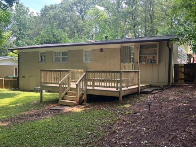 rear view of house featuring brick siding, fence, a wooden deck, and a lawn