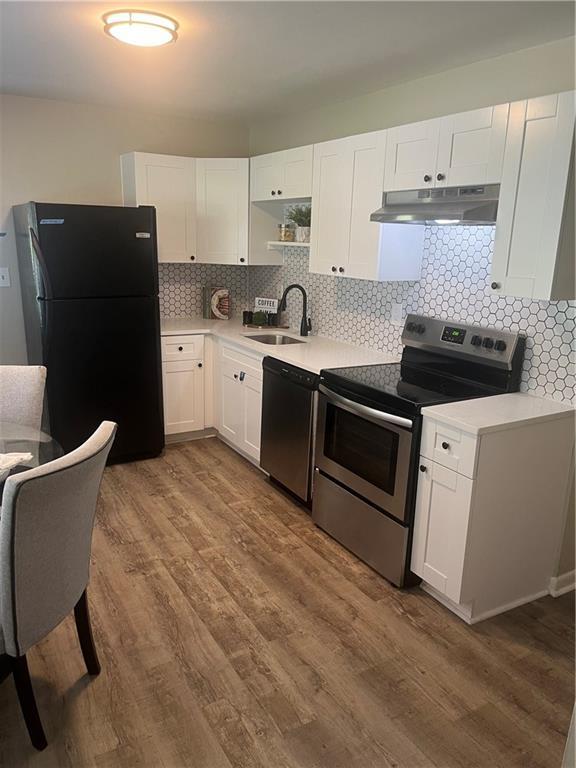 kitchen with dark wood-style floors, white cabinetry, a sink, under cabinet range hood, and black appliances