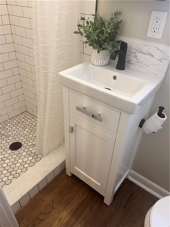 full bath with tasteful backsplash, toilet, a shower stall, vanity, and wood finished floors