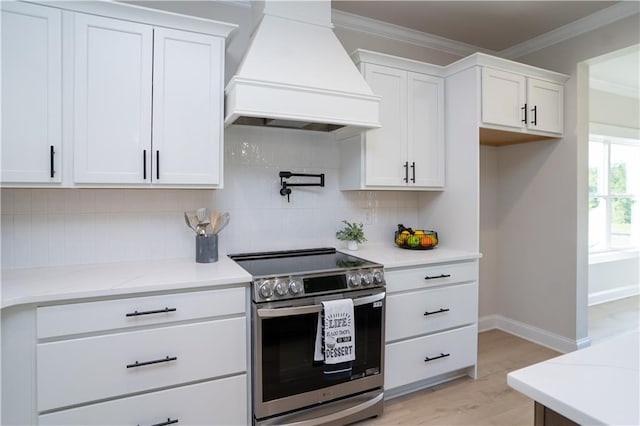 kitchen featuring stainless steel range with electric stovetop, premium range hood, white cabinets, light wood-type flooring, and tasteful backsplash