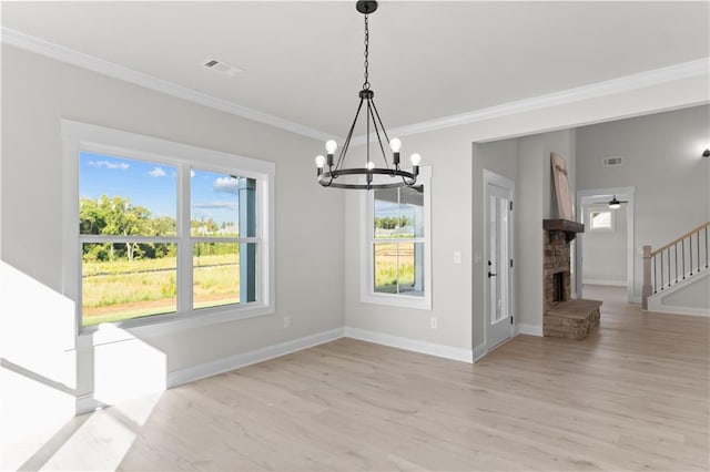 unfurnished dining area with an inviting chandelier, ornamental molding, a fireplace, and light hardwood / wood-style flooring