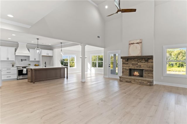 living room with ceiling fan, sink, high vaulted ceiling, light hardwood / wood-style floors, and a stone fireplace