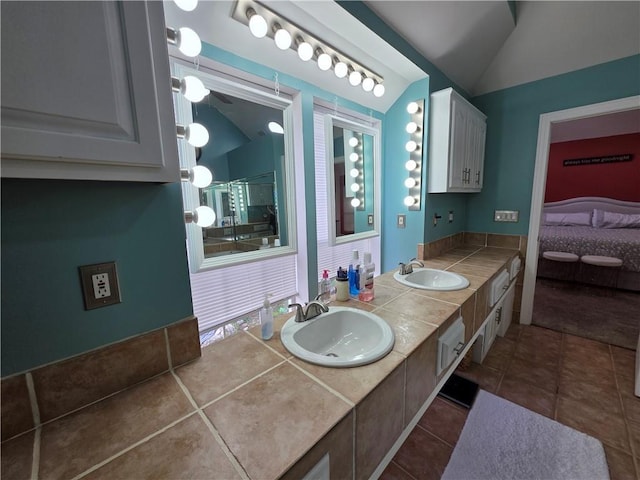 ensuite bathroom featuring tile patterned floors, double vanity, lofted ceiling, and a sink