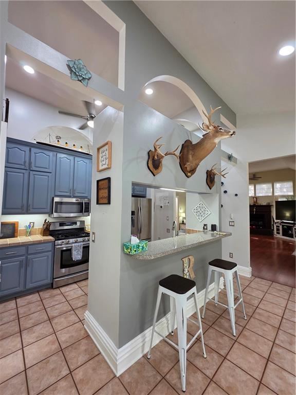 kitchen with blue cabinets, light tile patterned flooring, ceiling fan, and appliances with stainless steel finishes