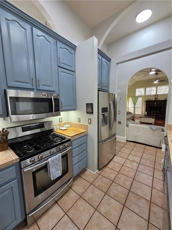 kitchen with stainless steel appliances, blue cabinets, arched walkways, light tile patterned flooring, and open floor plan