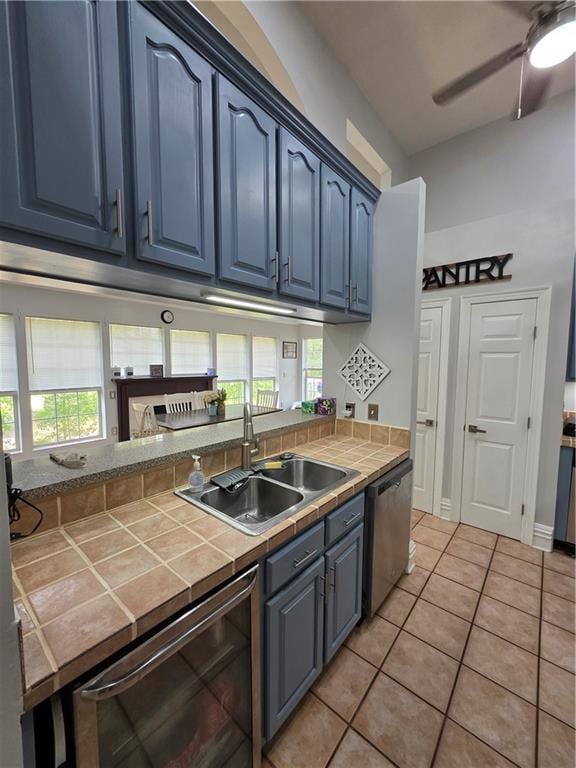 kitchen featuring blue cabinets, stainless steel dishwasher, plenty of natural light, a sink, and tile countertops