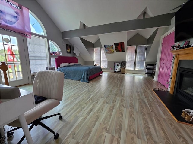 bedroom with high vaulted ceiling, access to outside, wood finished floors, and a glass covered fireplace