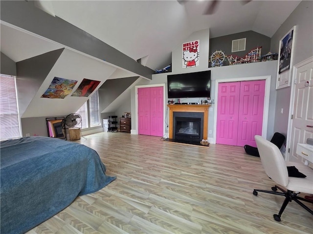 bedroom with visible vents, multiple closets, wood finished floors, and a glass covered fireplace