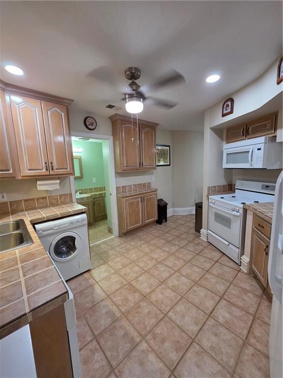 kitchen featuring white appliances, a sink, tile countertops, washer / dryer, and a ceiling fan