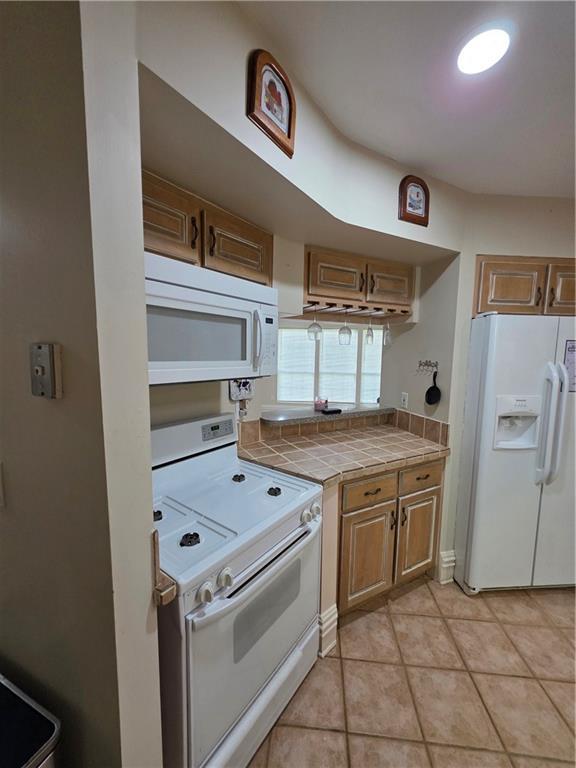 kitchen with light tile patterned floors, white appliances, and tile countertops