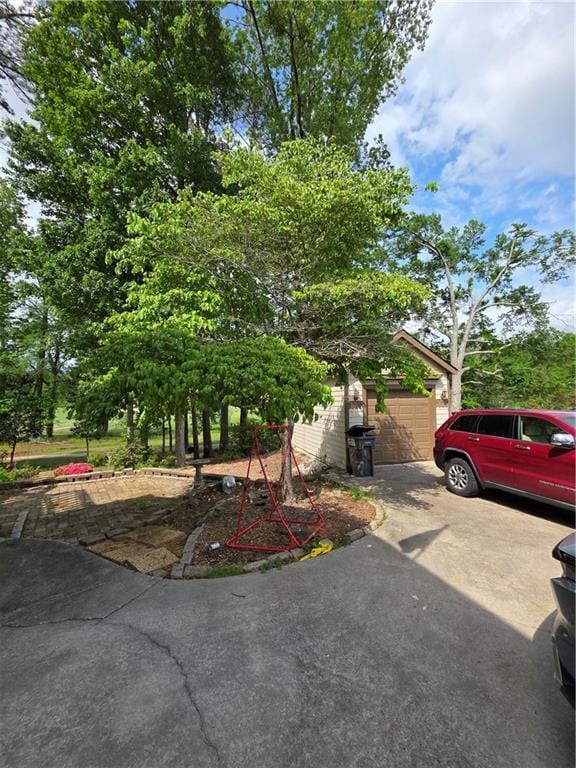 view of property hidden behind natural elements with a garage and concrete driveway